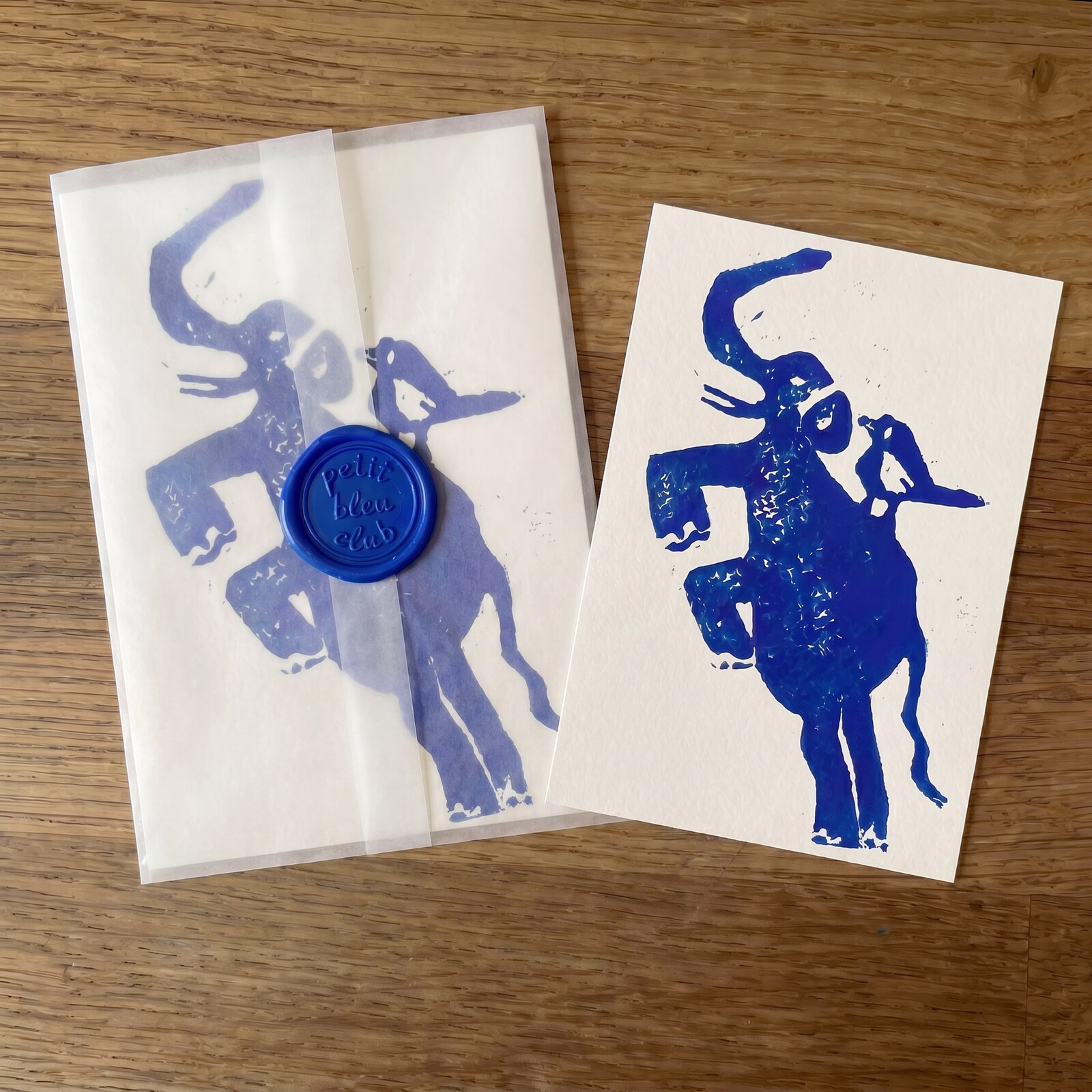Petit Bleu Club July 2026: hand-pulled blue elephant-with-bird print and a glassine envelope sealed with a Petit Bleu Club wax seal